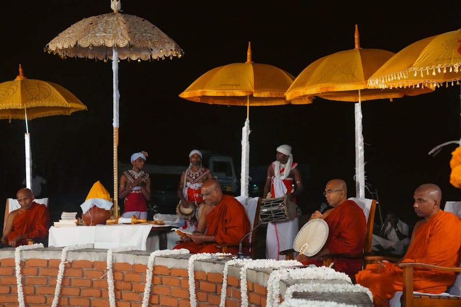 Theravada Buddhist monks gathered for a ceremonial ritual under decorative umbrellas in Sri Lanka.