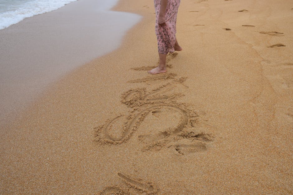 A woman strolls on Unawatuna Beach, Sri Lanka, with 'SUN' written in the sand, capturing a serene vacation moment.